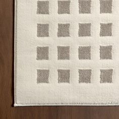 a white rug with squares and rectangles on top of wooden floor next to wall