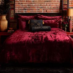 a bed with a red comforter and pillows on top of it next to a brick wall