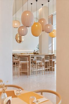 a dining room filled with lots of tables and chairs next to tall white walls covered in hanging lights