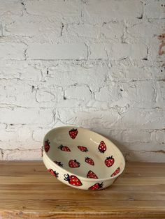 a white bowl with strawberries on it sitting on a wooden table next to a brick wall