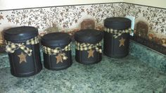 four black canisters sitting on top of a counter next to a wall with gold stars