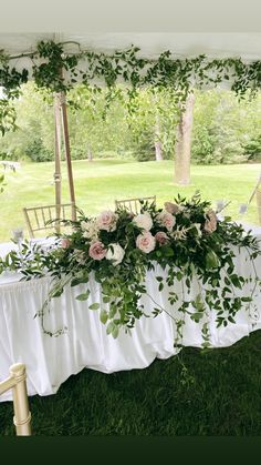 the table is covered with greenery and white linens for an outdoor wedding reception