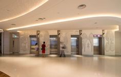 two people are standing in an empty lobby with doors and lights on the wall behind them