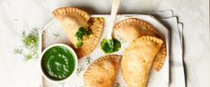 three empanada pastries on a white plate with a green dip in the middle