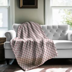 a white couch with a pink and grey checkered blanket on it in front of two windows