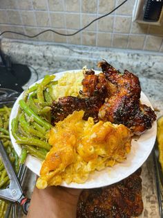 a person holding a plate full of food with meat and vegetables on the table next to it