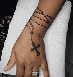 a person's hand with a rosary tattoo on the wrist and cross tattoos on it