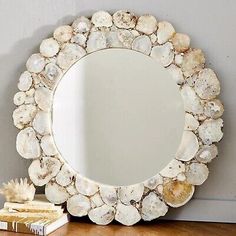 a mirror sitting on top of a wooden table next to a pile of seashells