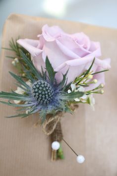 a pink rose and thistle flower bouquet on a piece of brown paper