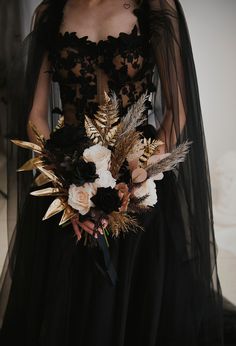 a woman in a black dress holding a bouquet with feathers on it's back