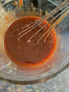 the sauce is being stirred in a glass bowl with metal whisks on top