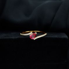 a gold ring with a red stone and white stones on it, sitting on a black velvet surface