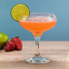 a drink in a wine glass with a lime slice and strawberries on the side