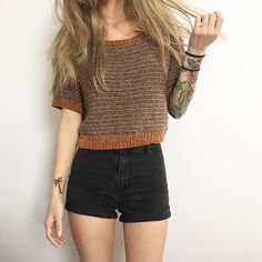 a woman with long hair standing in front of a white wall wearing black shorts and a knitted sweater