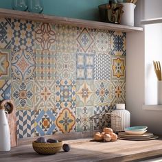 a kitchen counter topped with lots of plates and bowls next to a wall covered in colorful tiles