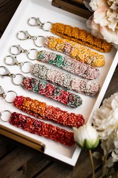 six keychains in different colors sitting on a white tray next to some flowers