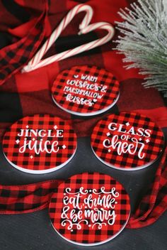 four red and black plaid buttons with white lettering on them, sitting next to a christmas tree