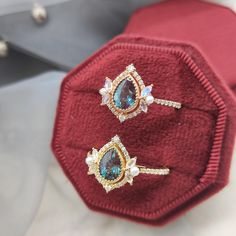 two rings are sitting on top of a red velvet case, one is blue and the other is white