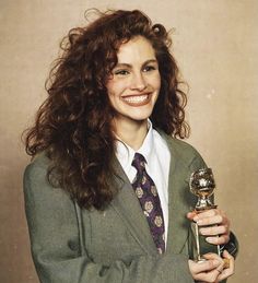 a woman with curly hair holding an award in her right hand and smiling at the camera