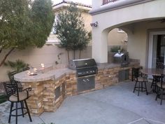 an outdoor kitchen with grill and bar stools