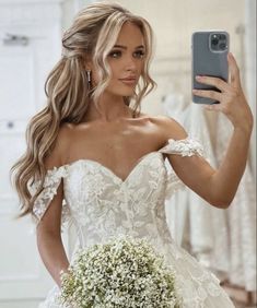 a woman in a wedding dress taking a selfie with her cell phone while holding a bouquet of baby's breath