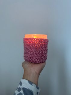 a hand holding a lit candle in front of a white wall with grey and pink designs