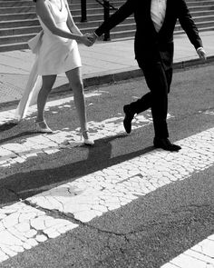 a man and woman walking across a crosswalk holding each other's hands in black and white