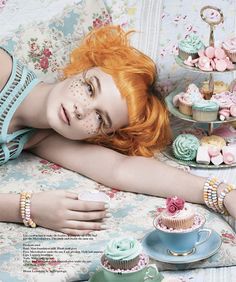 a woman laying on top of a couch next to cupcakes and cake dishes