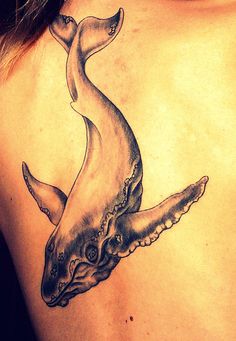 the back of a woman's shoulder with a whale tattoo on her left side