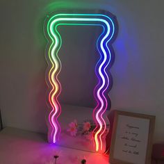 a mirror that has been lit up with neon lights and some flowers in front of it