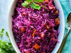 a white bowl filled with red cabbage and carrots next to a spoon on a blue towel