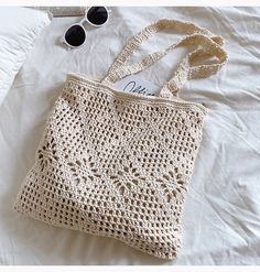 a crocheted bag sitting on top of a bed next to sunglasses and eyeglasses