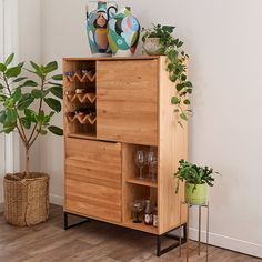 a wooden cabinet with wine glasses and plants in it next to a potted plant