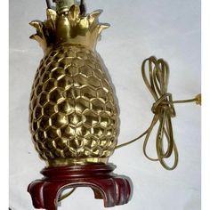 a gold pineapple lamp on a wooden base with a cord plugged into it