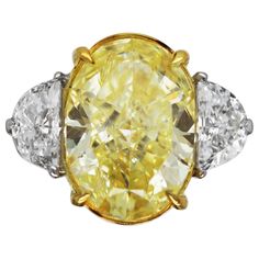 Three Stone Engagement Ring with GIA certified 5.40 carat Fancy Yellow Oval Cut Diamond center stone and two half moon side stones (0.92 TCW). Natural fancy yellow oval cut diamond with VS1 clarity set on 18k yellow gold and platinum. A perfectly proportioned 3 stone engagement ring featuring a richly colored, GIA certified, fancy yellow diamond. Fashioned into a brilliant oval cut, the pairing of half moon side stones fits seamlessly against the center stone. The side stones are E colored, with VS1 clarity and their combined weight is 0.92 carat. The setting, a mix of 18k yellow gold and platinum, is designed to emphasize the color of the center stone whilst offering a more modern look. As fancy colored diamonds are often cut to retain color, the open basket setting allows as much "fire” Half Moon Side Stones, 3 Stone Engagement Ring, Basket Setting, 3 Stone Engagement Rings, Three Stone Engagement Ring, Fancy Yellow Diamond, Stone Engagement Ring, Three Stone Engagement, Three Stone Engagement Rings