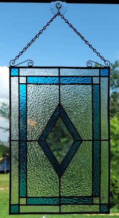 a stained glass window hanging from a chain on top of a grass covered field with trees in the background