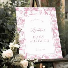 a baby shower sign with flowers and greenery in the foreground, on an easel