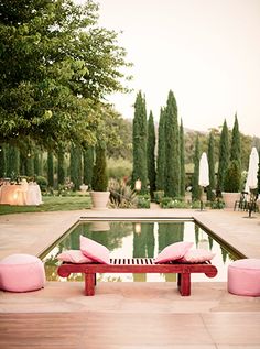 two pink pillows sitting on top of a wooden bench next to a large swimming pool