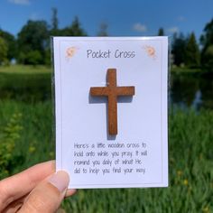 a person holding up a card with a wooden cross on it in front of some grass