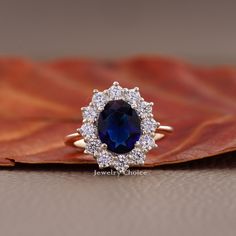 an oval shaped blue sapphire and diamond halo ring on top of a brown leather leaf