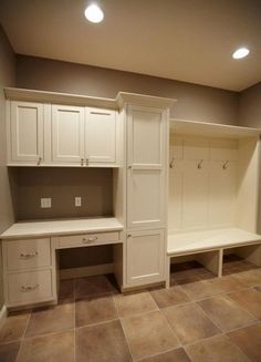 an empty mudroom with white cabinets and drawers on the wall, in front of a door