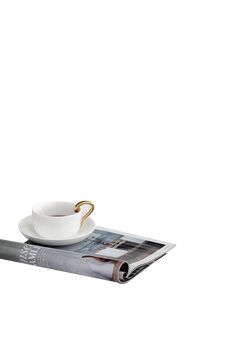 a coffee cup and saucer sitting on top of a magazine with a gold handle