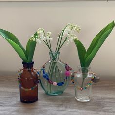 three vases with flowers in them sitting on a table next to each other and beaded bracelets