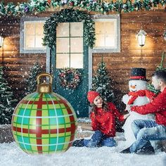 two people sitting in front of a christmas tree with a snowman on the ground