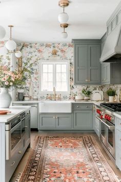 a kitchen with gray cabinets and floral wallpaper on the walls, an area rug in front of the sink