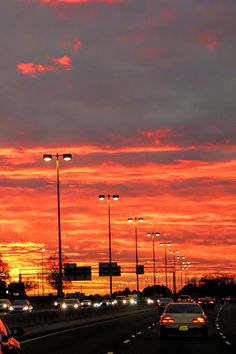 cars driving down the highway at sunset with street lights on either side and one car in the foreground