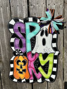 a sign that says spooky on the side of a wooden fence with halloween decorations