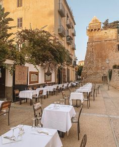 an outdoor dining area with tables and chairs in front of a stone wall, surrounded by tall buildings