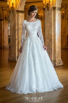 a woman in a white wedding dress standing on a wooden floor with columns and chandeliers