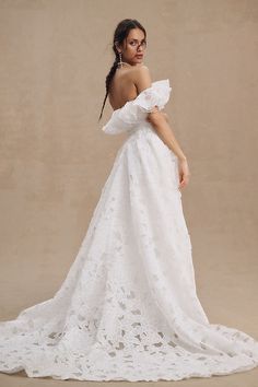 a woman in a white wedding dress standing with her back to the camera and looking off into the distance